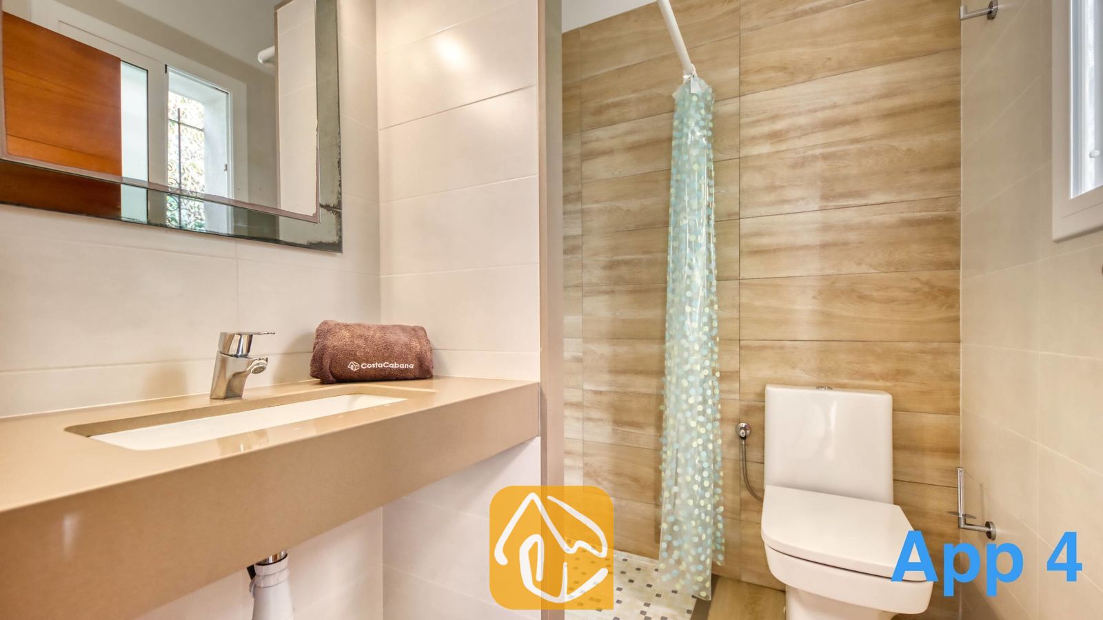 Vakantievilla's Costa Brava Spanje - Villa Pilar - Badkamer voorzien van een beige wastafelblad met een bruine handdoek, een toilet en een douche met wandtegels met een houtmotief en een gordijn met patroon