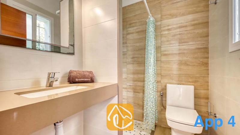 Villas de vacances Costa Brava Espagne - Villa Pilar - Salle de bains équipée d'un plan de toilette beige avec vasque et d'une serviette marron, de toilettes et d'une douche habillée de carrelage imitation bois et d'un rideau à motifs.