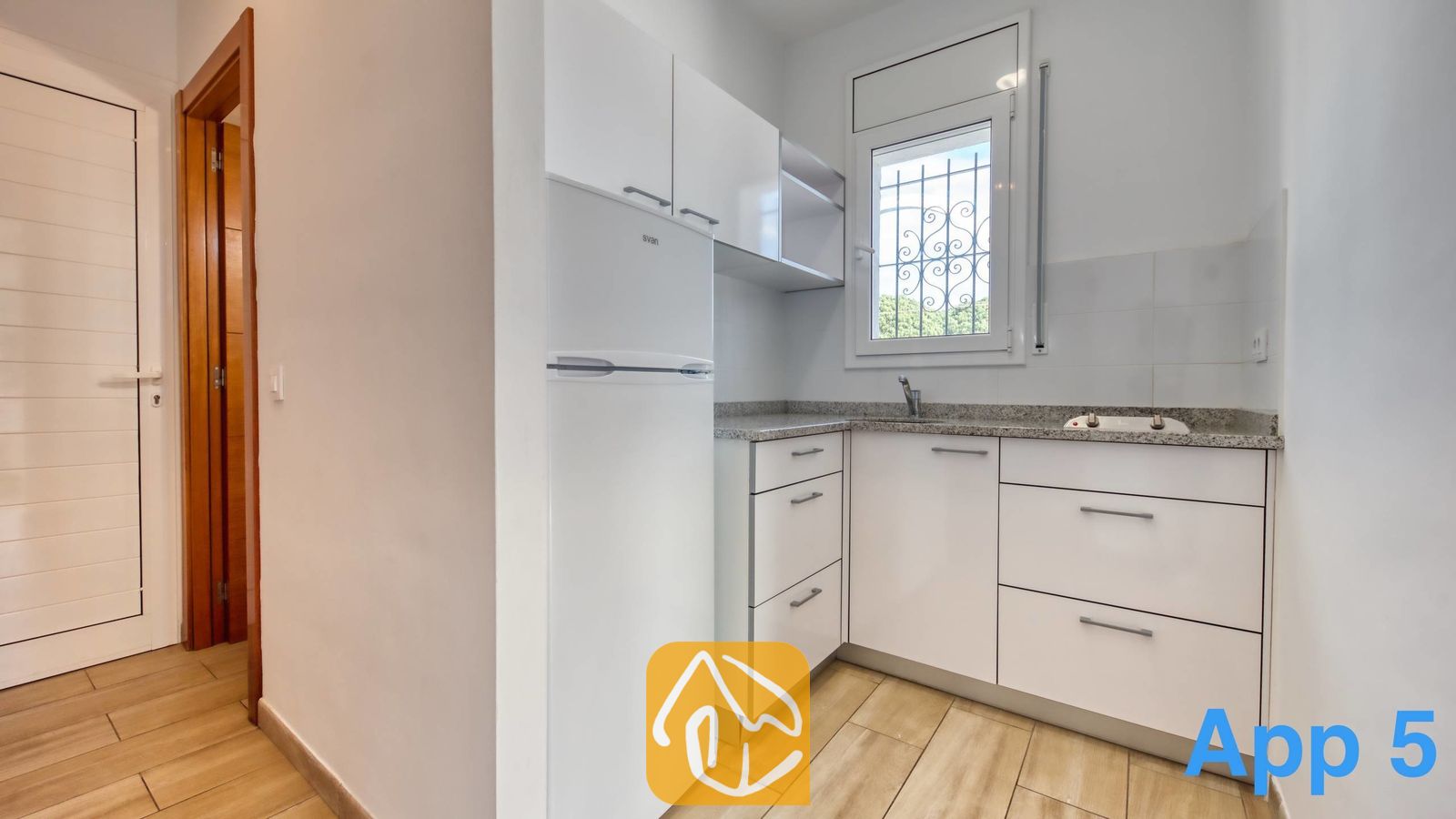 Vakantievilla's Costa Brava Spanje - Villa Pilar - Compacte witte keuken met glanzende kasten, stenen aanrechtbladen en een raam met rolluiken/veiligheidsroosters.