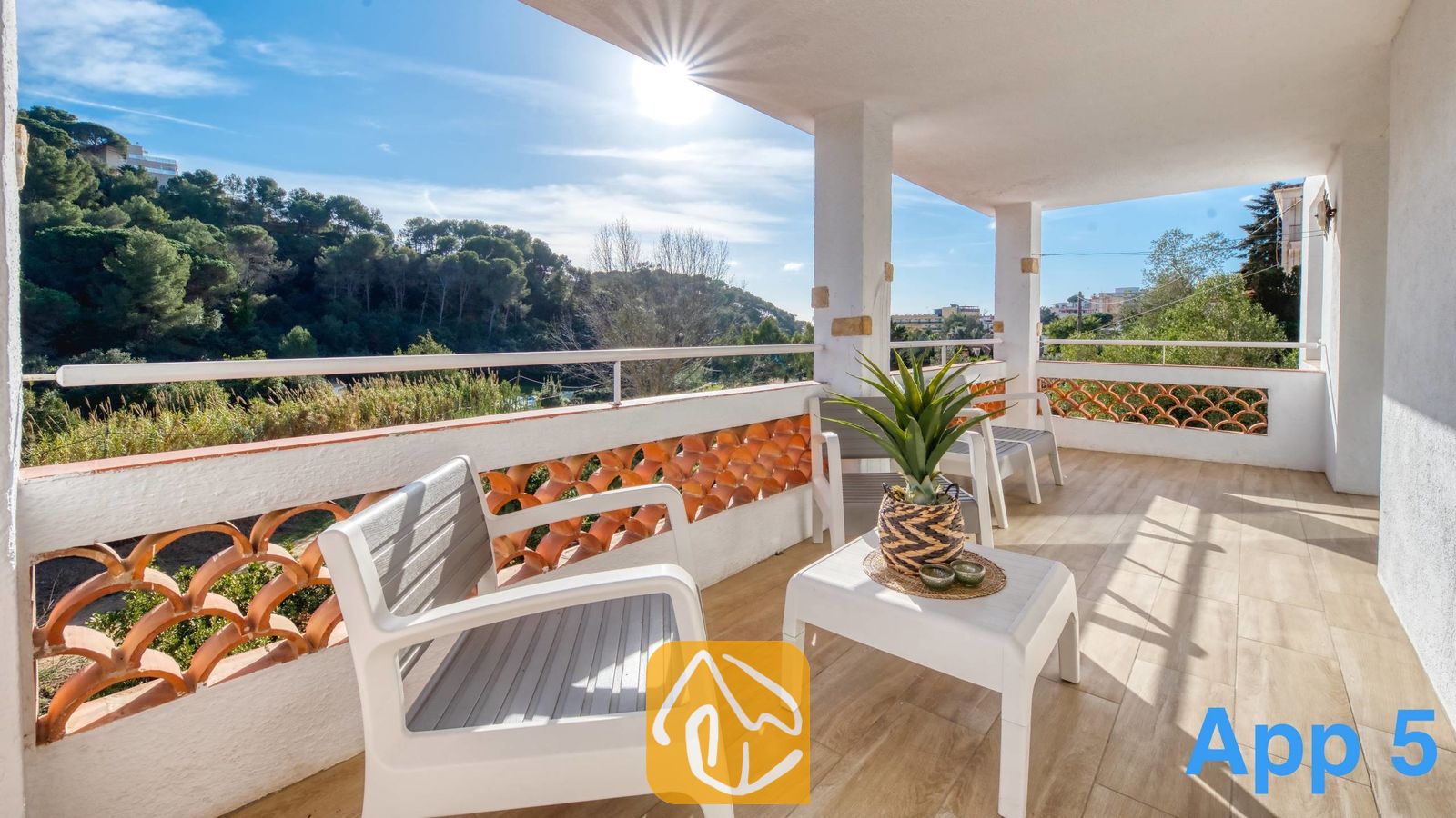 Vakantievilla's Costa Brava Spanje - Villa Pilar - Overdekt terras bij Villa Pilar met witte tuinstoelen, een tafeltje met een potplant en een balustrade met terracotta tegelpatronen die uitkijkt over groene heuvels.