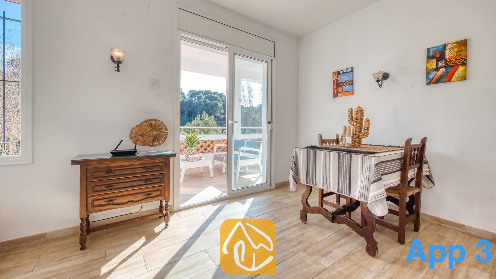 Vakantievilla's Costa Brava Spanje - Villa Pilar - Lichte eethoek in Villa Pilar met een houten tafel, een gestreepte tafelkleed en een glazen schuifdeur die uitkomt op een terras met uitzicht op het bos.