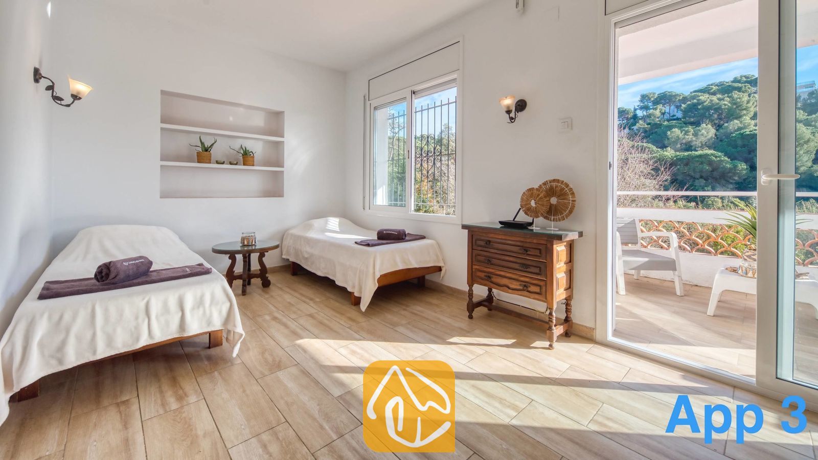 Vakantievilla's Costa Brava Spanje - Villa Pilar - Slaapkamer met twee eenpersoonsbedden, een houten commode en glazen schuifdeuren die uitkomen op een balkon met uitzicht op groene heuvels in de verte.
