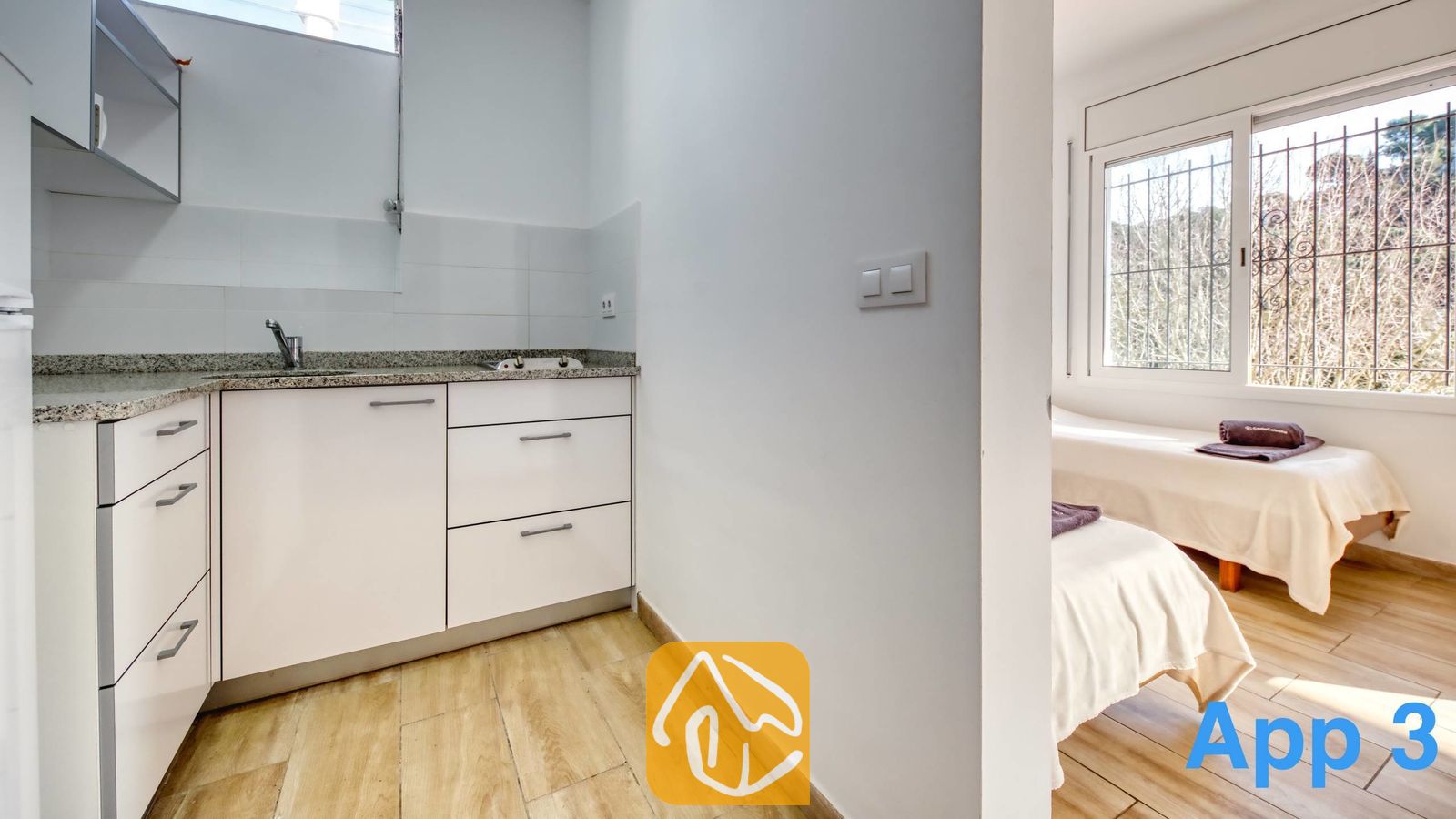 Vakantievilla's Costa Brava Spanje - Villa Pilar - Kleine kitchenette met witte kasten, granieten aanrechtbladen en een roestvrijstalen spoelbak, die overgaat in een slaapkamer met twee eenpersoonsbedden.