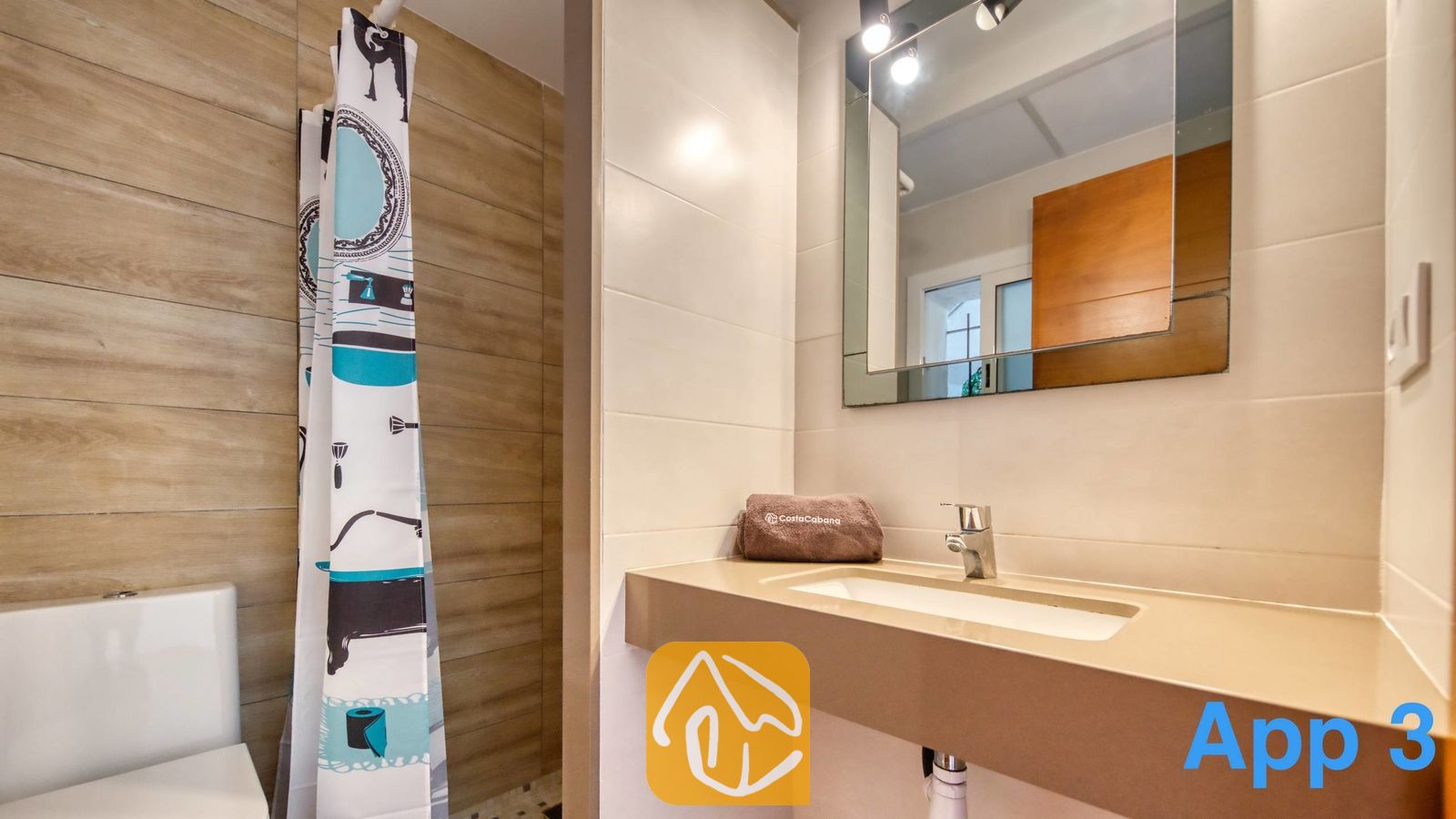 Vakantievilla's Costa Brava Spanje - Villa Pilar - Badkamer met een wastafel op een beige wastafelblad, een wandspiegel met bovenverlichting, een toilet en een gedessineerd douchegordijn.