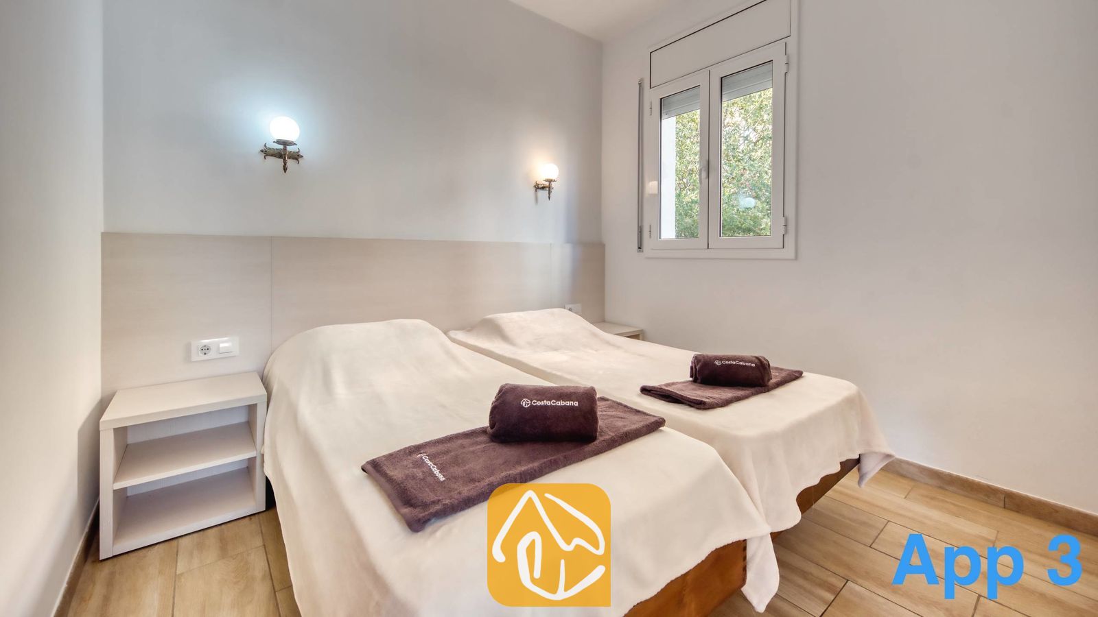 Vakantievilla's Costa Brava Spanje - Villa Pilar - Slaapkamer met twee eenpersoonsbedden voorzien van witte spreuken, opgevouwen bruine handdoeken, houten nachtkastjes en wandlampen in de vorm van een wereldbol.