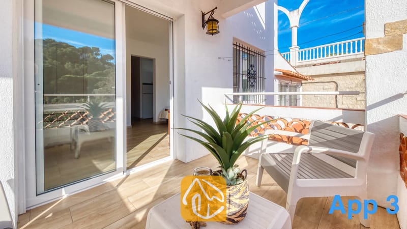 Villas de vacances Costa Brava Espagne - Villa Pilar - Ensoleillé, le balcon de la Villa Pilar dispose d'un fauteuil blanc, d'une petite table avec une plante en pot et d'une porte-fenêtre coulissante s'ouvrant sur l'intérieur.