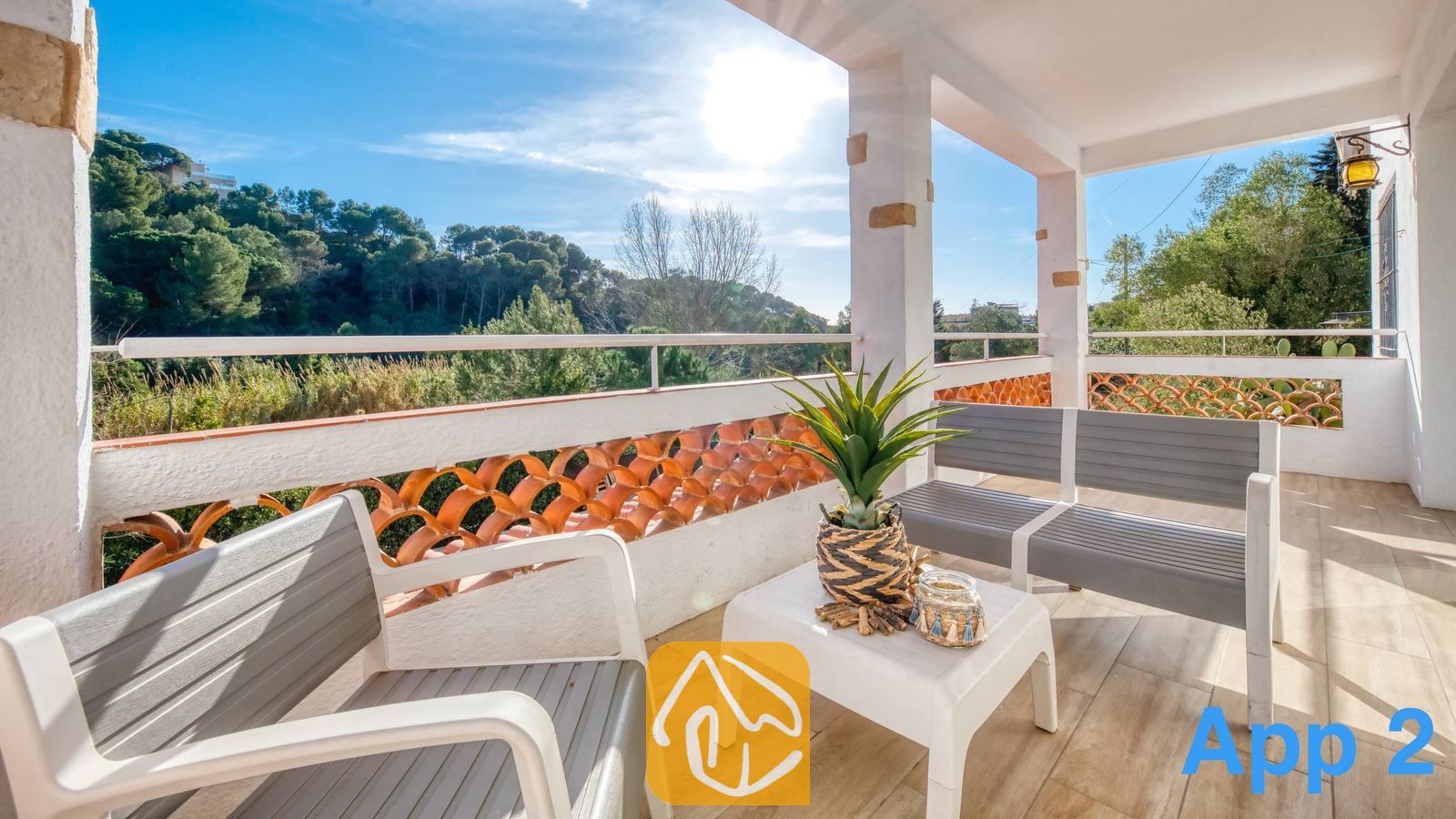 Vakantievilla's Costa Brava Spanje - Villa Pilar - Terras van Villa Pilar met een grijze buitenlounge, een klein wit tafeltje met een in een pot geplaatste plant, en een balustrade met uitzicht op groene heuvels.