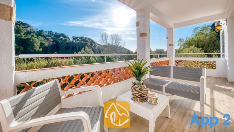 Villas de vacances Costa Brava Espagne - Villa Pilar - Terrasse de la Villa Pilar dotée d'un salon de jardin gris, d'une petite table blanche avec une plante en pot et d'un garde-corps surplombant des collines verdoyantes.