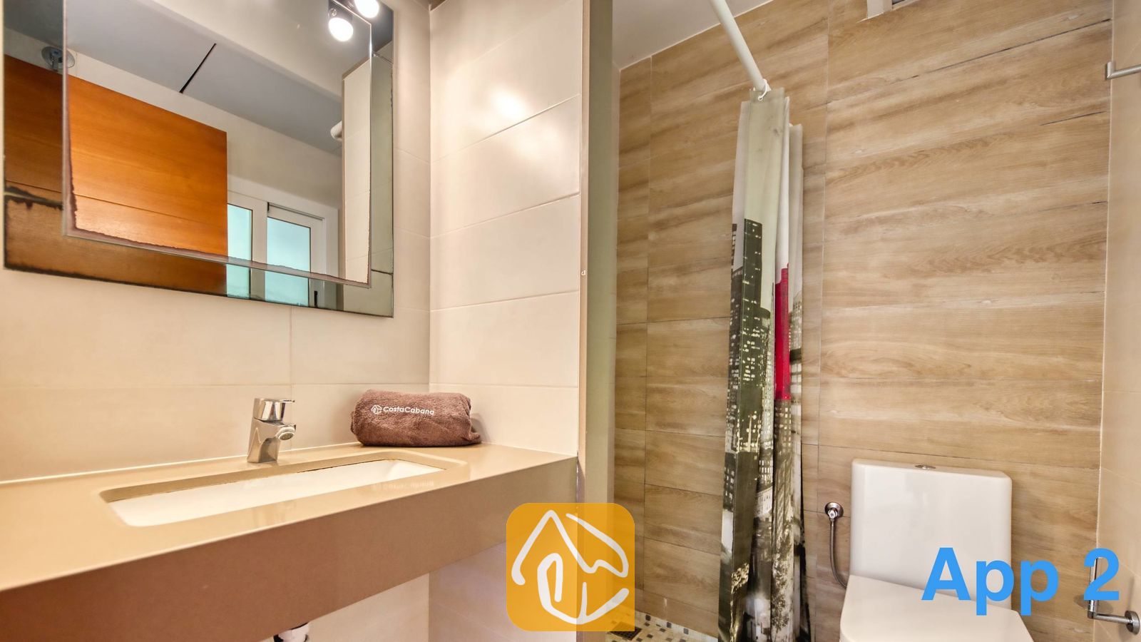 Vakantievilla's Costa Brava Spanje - Villa Pilar - Moderne badkamer met een beige wastafel op blad, een rechthoekige wandspiegel en een toilet naast een douche met een gordijn met patroon.