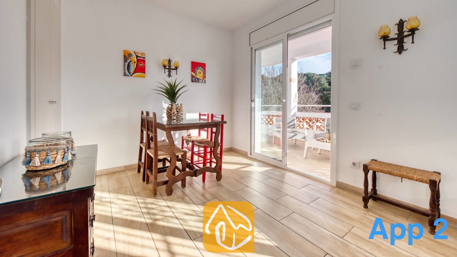 Vakantievilla's Costa Brava Spanje - Villa Pilar - Eethoek in Villa Pilar met houten meubels, tegelvloeren, kleurrijke muurkunst en glazen schuifdeuren die uitkomen op een zonnig balkon.