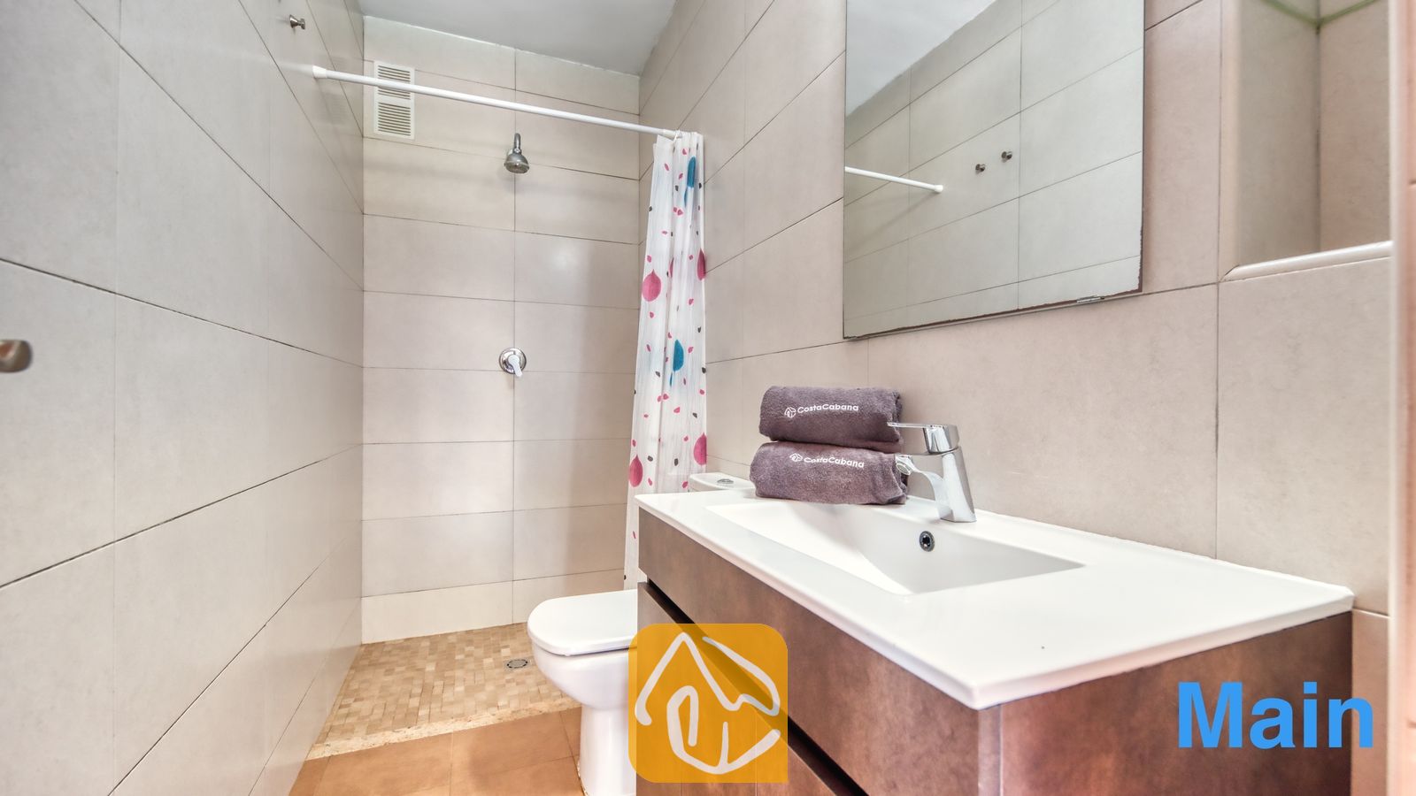 Vakantievilla's Costa Brava Spanje - Villa Pilar - Moderne badkamer met betegelde muren in een beigetint, een wit badkamermeubel met opgevouwen handdoeken, een toilet en een inloopdouche met een gedessineerd gordijn.