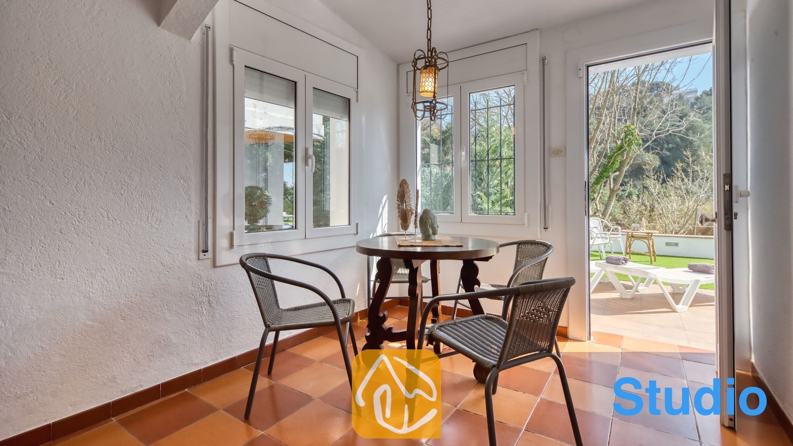 Vakantievilla's Costa Brava Spanje - Villa Pilar - Lichte serre bij Villa Pilar met een donkerhouten eettafel, vier gevlochten stoelen, terracotta vloertegels en open glazen deuren die leiden naar een terras.
