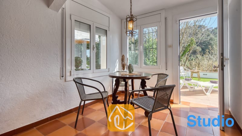Villas de vacances Costa Brava Espagne - Villa Pilar - Lumineuse véranda à la Villa Pilar dotée d'une table de salle à manger en bois foncé, de quatre chaises tressées, de sols en carrelage en terre cuite et de portes vitrées coulissantes ouvrant sur une terrasse.