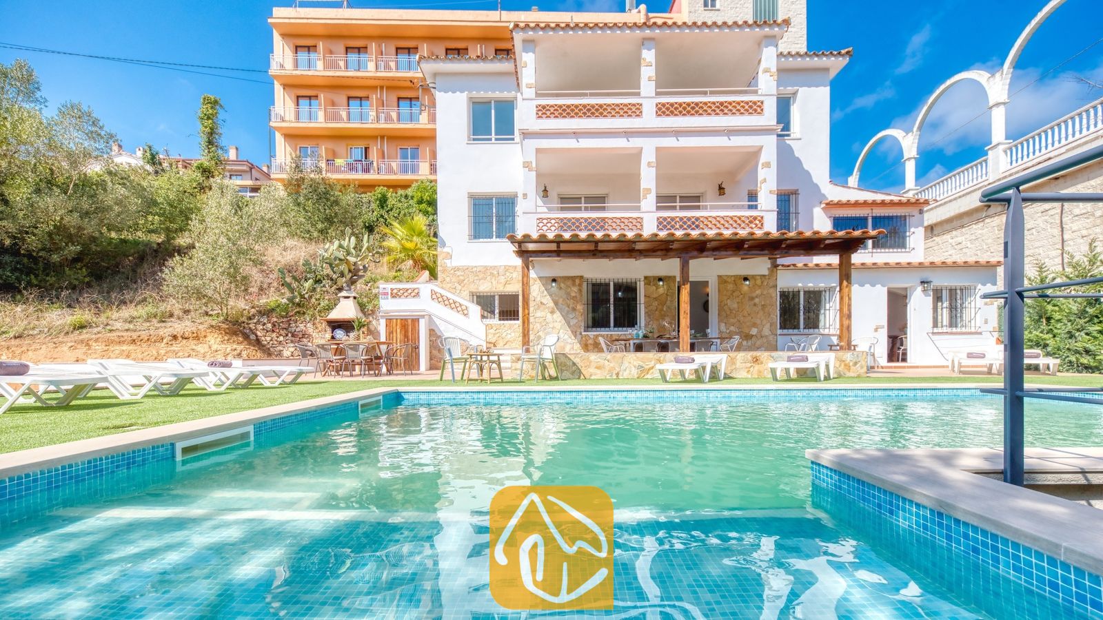 Vakantievilla's Costa Brava Spanje - Villa Pilar - Privézwembad en de exterieur met meerdere niveken van Villa Pilar in Spanje, gekenmerkt door witte muren, balkons met terracotta tegels en diverse ligstoelen op het gras.