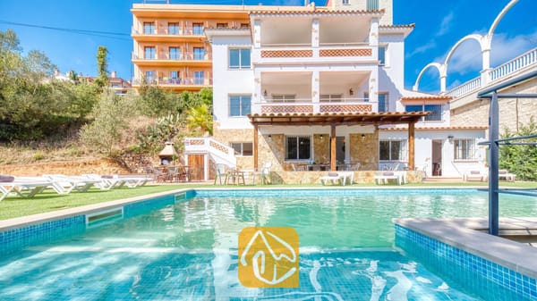 Vakantievilla's Costa Brava Spanje - Villa Pilar - Privézwembad en de exterieur met meerdere niveken van Villa Pilar in Spanje, gekenmerkt door witte muren, balkons met terracotta tegels en diverse ligstoelen op het gras.