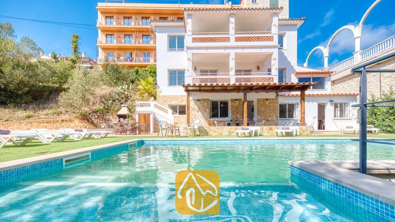 Vakantievilla's Costa Brava Spanje - Villa Pilar - Privézwembad en de exterieur met meerdere niveken van Villa Pilar in Spanje, gekenmerkt door witte muren, balkons met terracotta tegels en diverse ligstoelen op het gras.