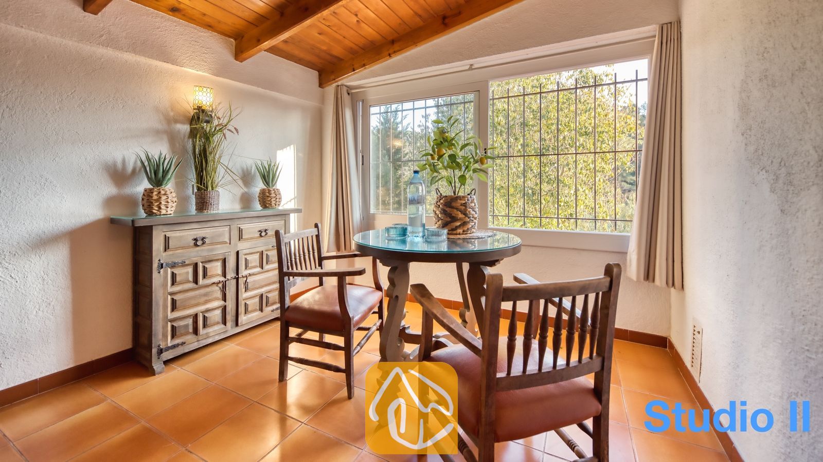 Vakantievilla's Costa Brava Spanje - Villa Pilar - Houten eettafel met met leer beklede stoelen, opgesteld bij een groot raam met uitzicht op het groene bladerdak bij Villa Pilar.