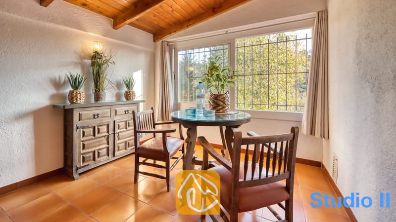 Villas de vacances Costa Brava Espagne - Villa Pilar - À la Villa Pilar, table à manger en bois avec des chaises aux coussins en cuir, installée près d'une grande fenêtre offrant une vue sur un feuillage verdoyant.