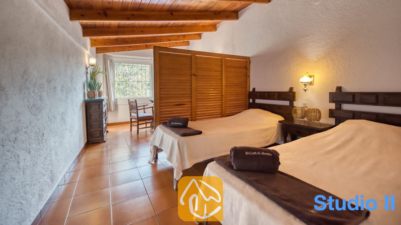 Vakantievilla's Costa Brava Spanje - Villa Pilar - Slaapkamer met twee eenpersoonsbedden, voorzien van donkerhouten hoofdborden, tegelvloeren en authentieke houten plafondbalken bij Villa Pilar.