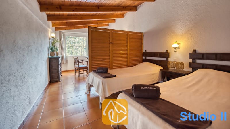 Villas de vacances Costa Brava Espagne - Villa Pilar - Chambre de la Villa Pilar dotée de deux lits jumeaux avec têtes de lit en bois foncé, de sols carrelés et de poutres apparentes au plafond.