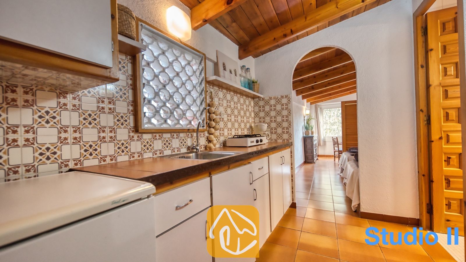 Vakantievilla's Costa Brava Spanje - Villa Pilar - Interieur van de keuken in Villa Pilar met een betegelde achterwand met motief, houten plafondbalken en tegelwerkanrechtbladen voorzien van een spoelbak en kookplaat.