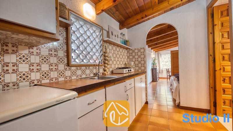 Villas de vacances Costa Brava Espagne - Villa Pilar - Intérieur de la cuisine de la Villa Pilar, comprenant une crédence en carrelage à motifs, des poutres en bois au plafond et des plans de travail en carrelage équipés d'un évier et d'une plaque de cuisson.