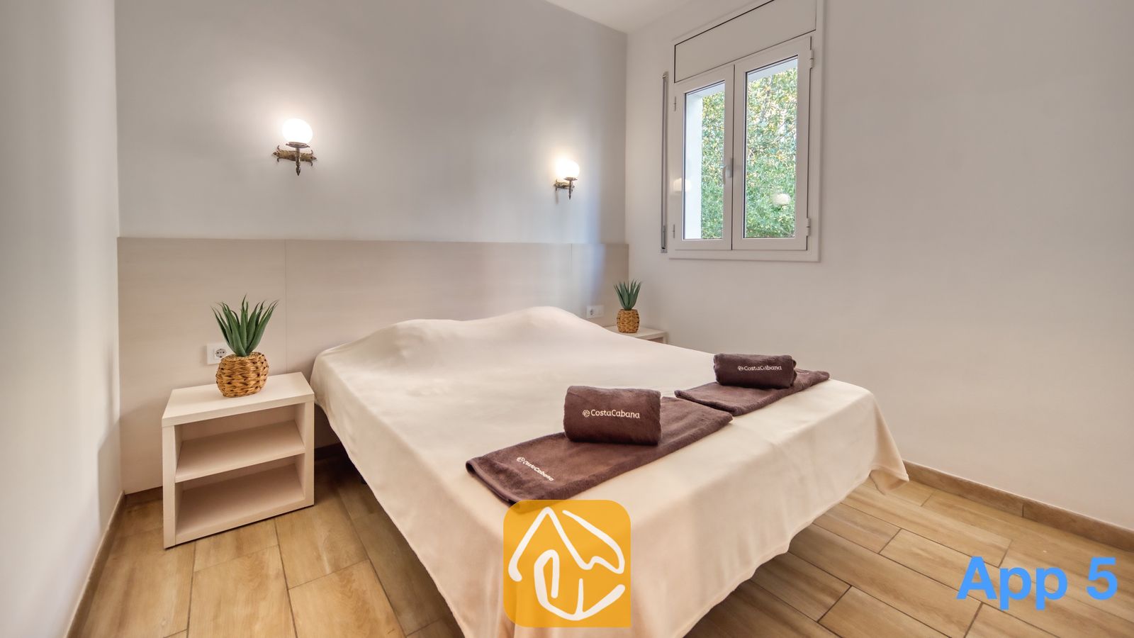 Vakantievilla's Costa Brava Spanje - Villa Pilar - Slaapkamer met een tweepersoonsbed, twee nachtkastjes met in pot geplante planten, wandlampen en een raam met uitzicht op groen loof.