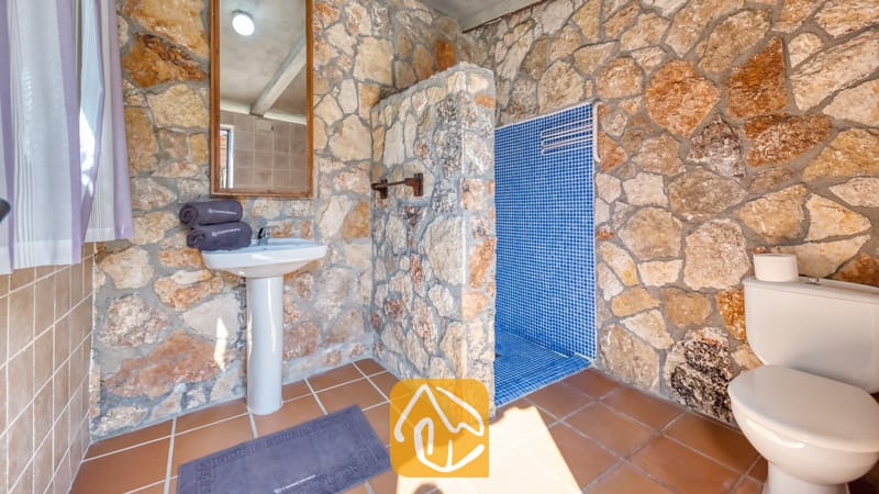 Vakantievilla's Costa Brava Spanje - Villa Alba - Badkamer met rustieke stenen muren, een witte zuilwastafel, een betegelde doucheruimte met blauwe mozaïeken en bruine vloertegels.