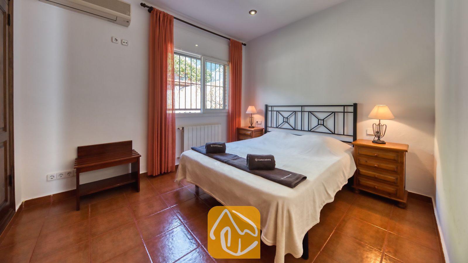 Vakantievilla's Costa Brava Spanje - Villa Alba - Slaapkamer met een tweepersoonsbed, een donker metalen frame, oranje gordijnen die het raam omlijsten, en twee houten nachtkastjes met lampen.