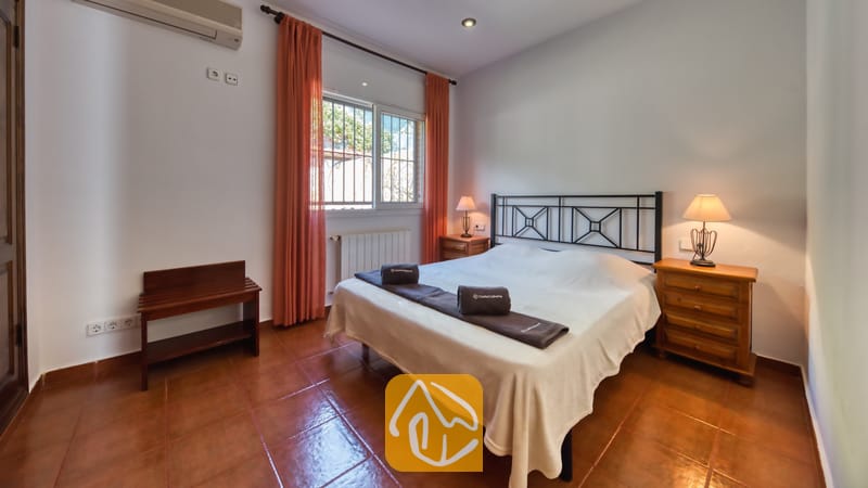 Vakantievilla's Costa Brava Spanje - Villa Alba - Slaapkamer met een tweepersoonsbed, een donker metalen frame, oranje gordijnen die het raam omlijsten, en twee houten nachtkastjes met lampen.