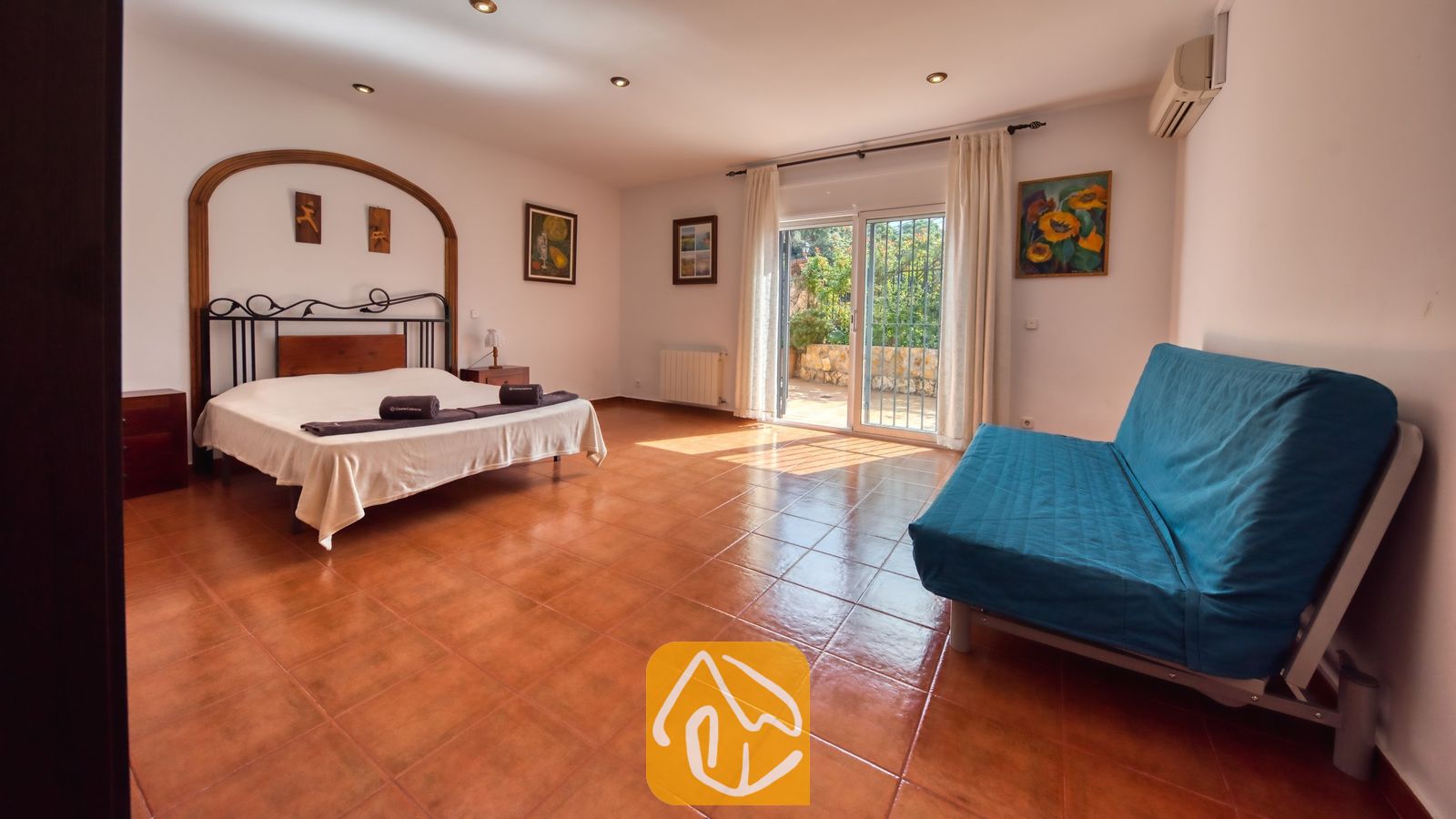 Vakantievilla's Costa Brava Spanje - Villa Alba - Ruime slaapkamer in Villa Alba met een tweepersoonsbed, een donker metalen frame, een blauwe bank en glazen schuifpui die toegang biedt tot een buitenterras.