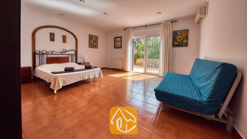 Vakantievilla's Costa Brava Spanje - Villa Alba - Ruime slaapkamer in Villa Alba met een tweepersoonsbed, een donker metalen frame, een blauwe bank en glazen schuifpui die toegang biedt tot een buitenterras.