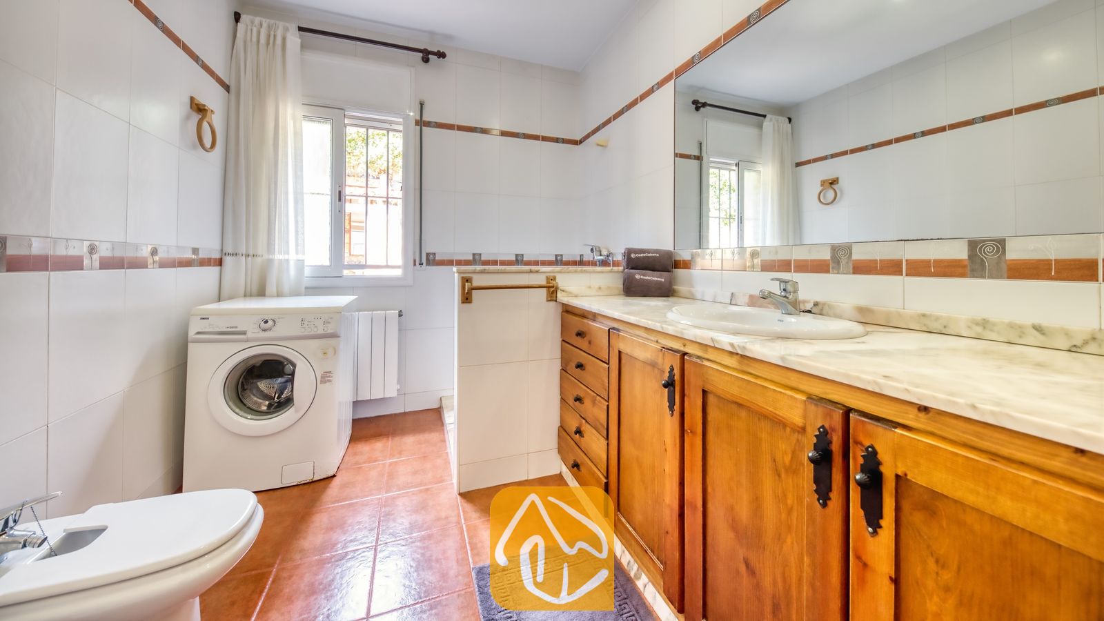 Vakantievilla's Costa Brava Spanje - Villa Alba - Lichte, betegelde badkamer met een houten badkamermeubel met een marmeren blad, een witte wasmachine en terracotta vloertegels.