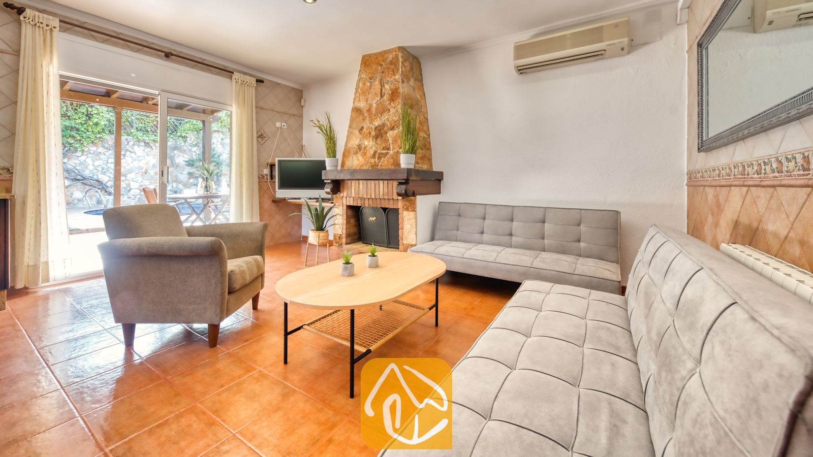 Vakantievilla's Costa Brava Spanje - Villa Alba - Woonkamer van Villa Alba met twee grijze Chesterfield-banken, een fauteuil, een ovale houten salontafel en een stenen open haard.
