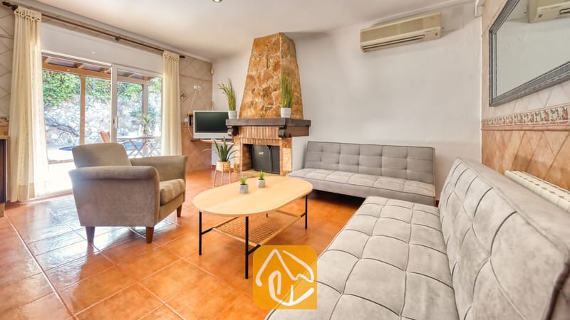 Vakantievilla's Costa Brava Spanje - Villa Alba - Woonkamer van Villa Alba met twee grijze Chesterfield-banken, een fauteuil, een ovale houten salontafel en een stenen open haard.