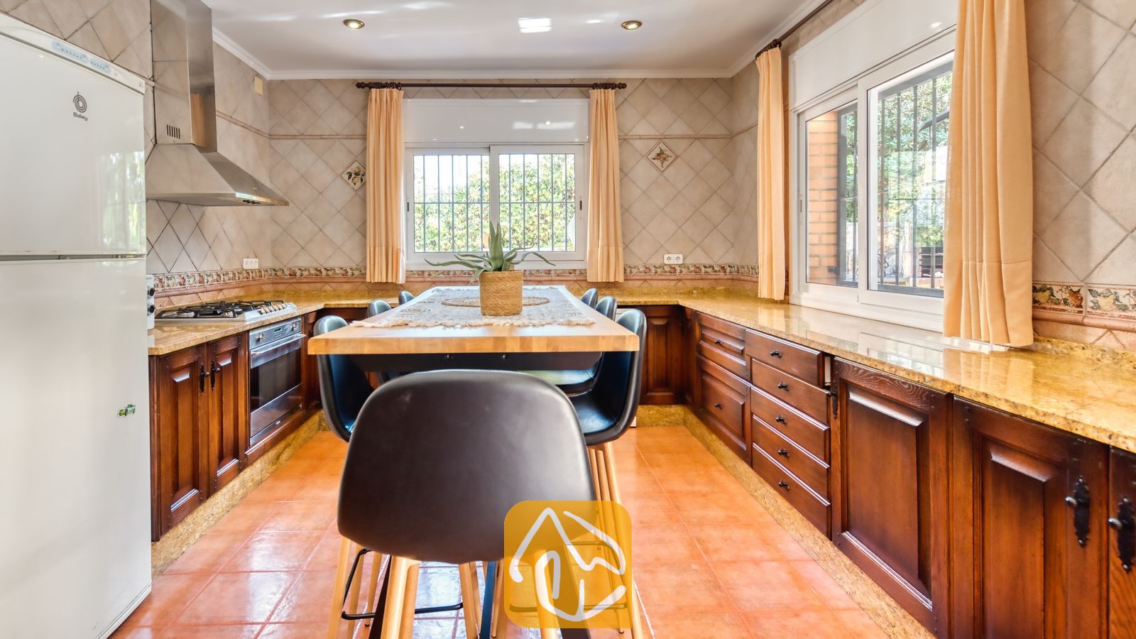 Vakantievilla's Costa Brava Spanje - Villa Alba - Ruime keuken met donkerhouten kasten, granieten aanrechtbladen, een centrale houten eettafel met zwarte stoelen en terracotta vloertegels.