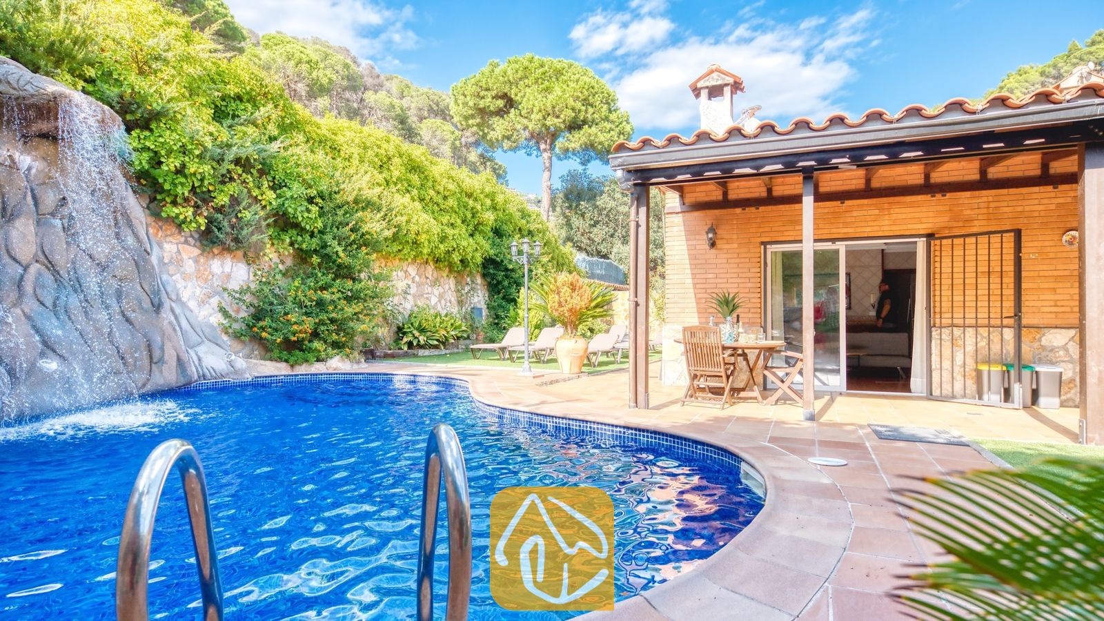 Vakantievilla's Costa Brava Spanje - Villa Alba - Privézwembad met een natuurstenen waterval bij Villa Alba, met een bakstenen terras, houten eethuismeubilair en een pannendak.