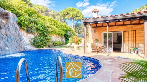 Vakantievilla's Costa Brava Spanje - Villa Alba - Privézwembad met een natuurstenen waterval bij Villa Alba, met een bakstenen terras, houten eethuismeubilair en een pannendak.
