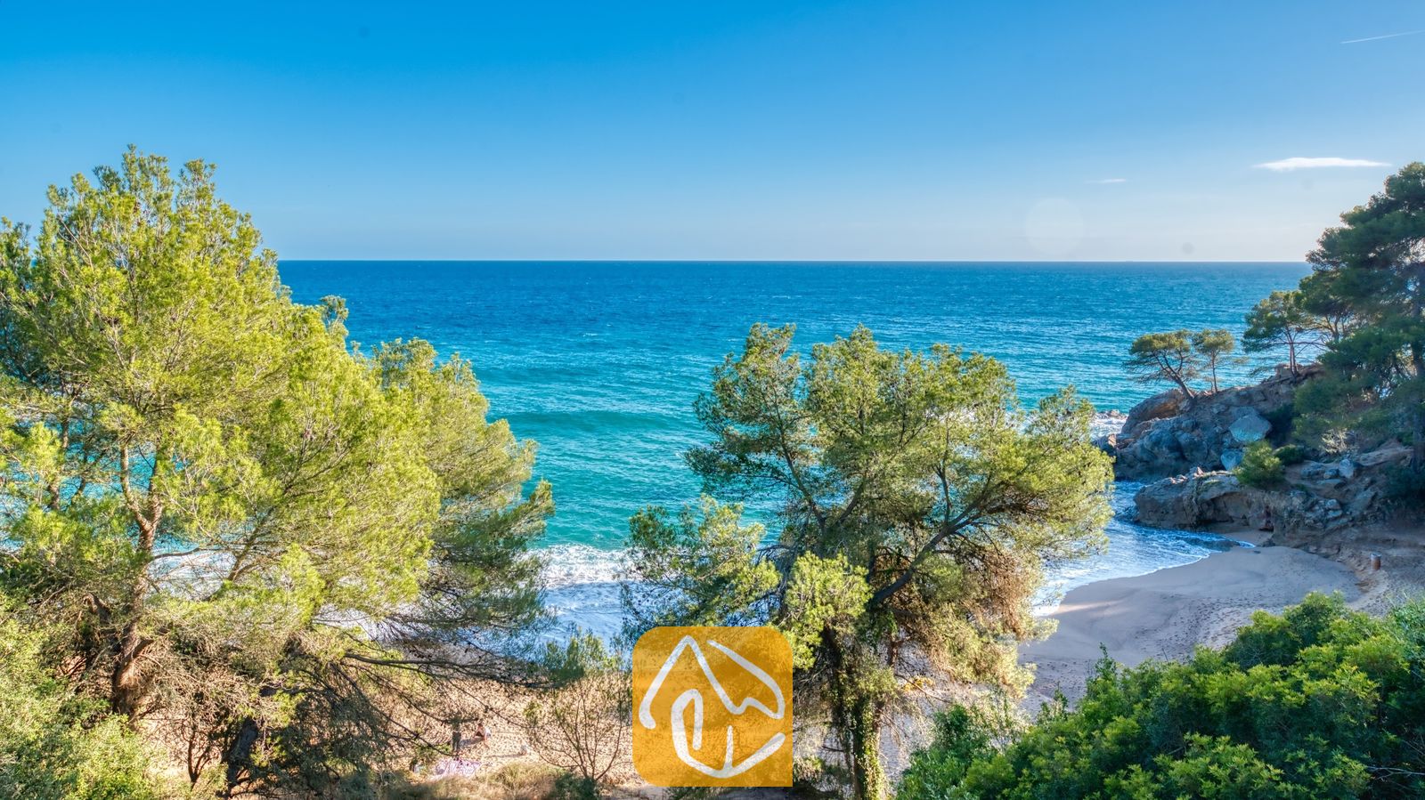 Vakantievilla's Costa Brava Spanje - Villa Santa Cristina - Een afgelegen zandbaai, omlijst door groene dennenbomen nabij Villa Santa Cristina, met azuurblauw zeewater en rotsachtige kliffen onder een stralende hemel.