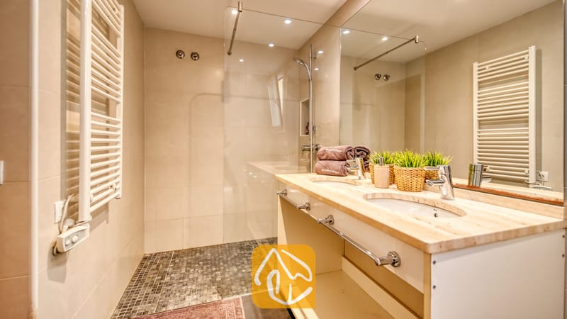 Villas de vacaciones Costa Brava España - Villa Santa Cristina - Baño equipado con tocador doble con dos lavabos, un espejo de gran tamaño y una ducha a ras de suelo con mampara de cristal y suelo de mosaico oscuro.