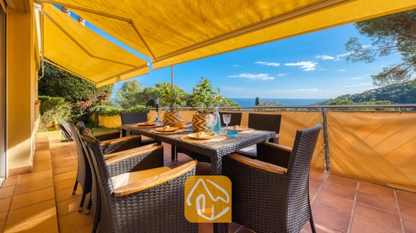 Vakantievilla's Costa Brava Spanje - Villa Santa Cristina - Terras met uitzicht op zee bij Villa Santa Cristina, voorzien van een eettafel voor zes personen, gele uitvalschermen en een vloer van terracotta tegels.
