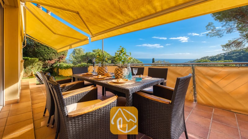 Vakantievilla's Costa Brava Spanje - Villa Santa Cristina - Terras met uitzicht op zee bij Villa Santa Cristina, voorzien van een eettafel voor zes personen, gele uitvalschermen en een vloer van terracotta tegels.