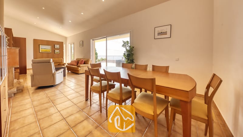 Vakantievilla's Costa Brava Spanje - Villa Mauri - Ruime woon- en eetkamer in Villa Mauri, voorzien van een houten eettafel met stoelen, tegelvloeren en glazen schuifdeuren die opengaan naar een balkon.