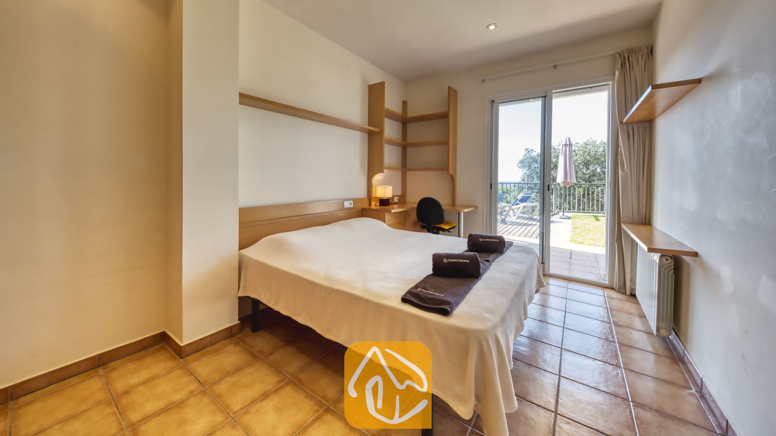 Vakantievilla's Costa Brava Spanje - Villa Mauri - Slaapkamer met een tweepersoonsbed, ingebouwde houten planken en glazen schuifdeuren die uitkomen op een zonnig buitenterras.