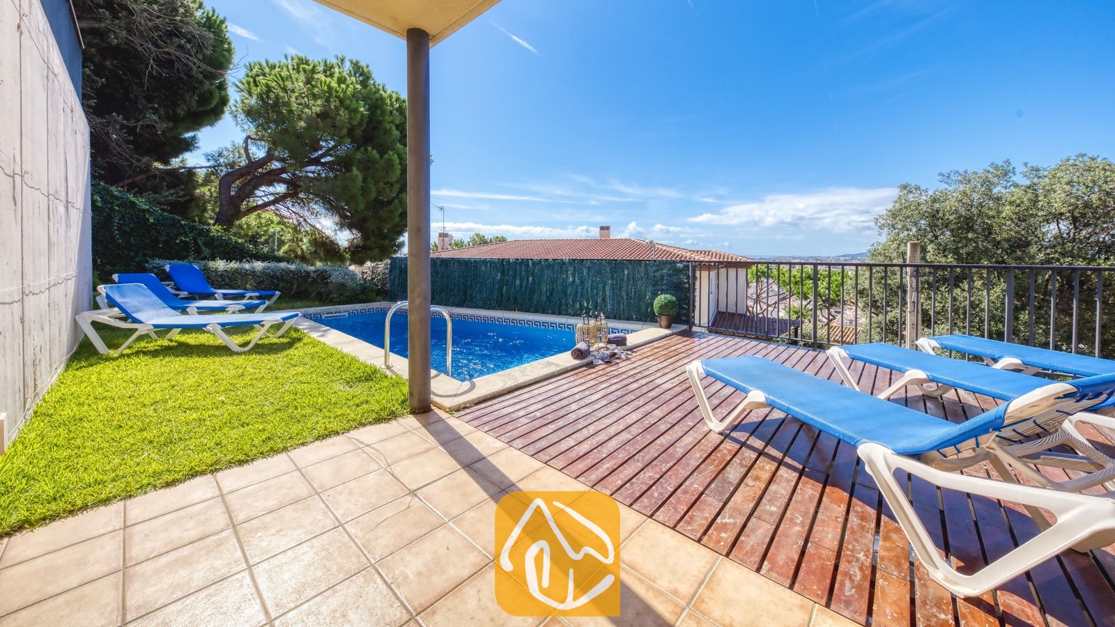 Vakantievilla's Costa Brava Spanje - Villa Mauri - Buiten terras van Villa Mauri met een zwembad, houten vlonders, blauwe ligbedden en groen gras onder een helderblauwe hemel