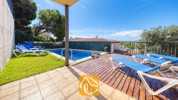 Vakantievilla's Costa Brava Spanje - Villa Mauri - Buiten terras van Villa Mauri met een zwembad, houten vlonders, blauwe ligbedden en groen gras onder een helderblauwe hemel