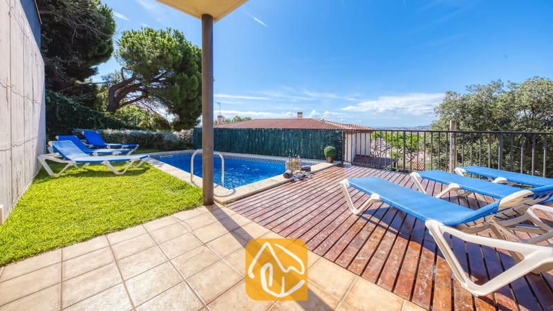 Vakantievilla's Costa Brava Spanje - Villa Mauri - Buiten terras van Villa Mauri met een zwembad, houten vlonders, blauwe ligbedden en groen gras onder een helderblauwe hemel