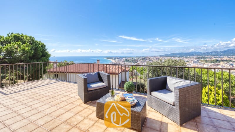 Vakantievilla's Costa Brava Spanje - Villa Mauri - Terras met uitzicht op zee en het stadje vanaf Villa Mauri, ingericht met donkerkleurige rieten fauteuils en een bijpassende salontafel op een tegelvloer.