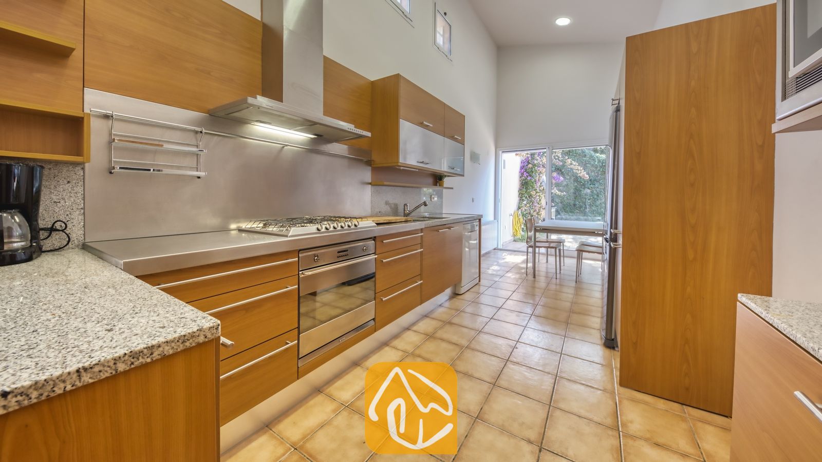 Vakantievilla's Costa Brava Spanje - Villa Mauri - Moderne keuken met houten kasten, roestvrijstalen apparatuur, granieten aanrechtbladen en tegelvloeren die toegang biedt tot een terrasdeur.