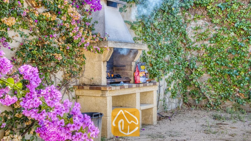 Vakantievilla's Costa Brava Spanje - Villa Mauri - Stenen buitenbarbecue bij Villa Mauri, prachtig gelegen tegen een muur begroeid met groene klimop en felpaarse bougainville.